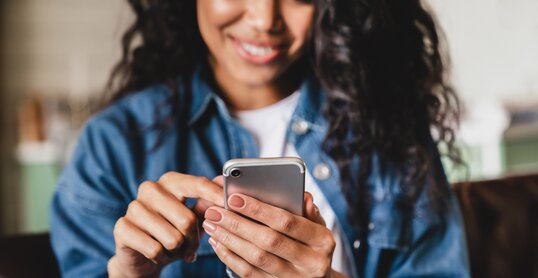 Cropped shot of an african-american young woman using smart phone at home. Smiling african american woman using smartphone at home, messaging or browsing social networks while relaxing on couch