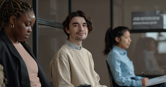 Portrait of young candidate sitting in waiting room with resume and looking at camera