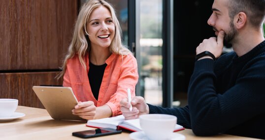 Cheerful caucasian female student looking a her male friend discussing learning project on cafe break, prosperous young man and woman employees talking to each other about business ideas on meeting